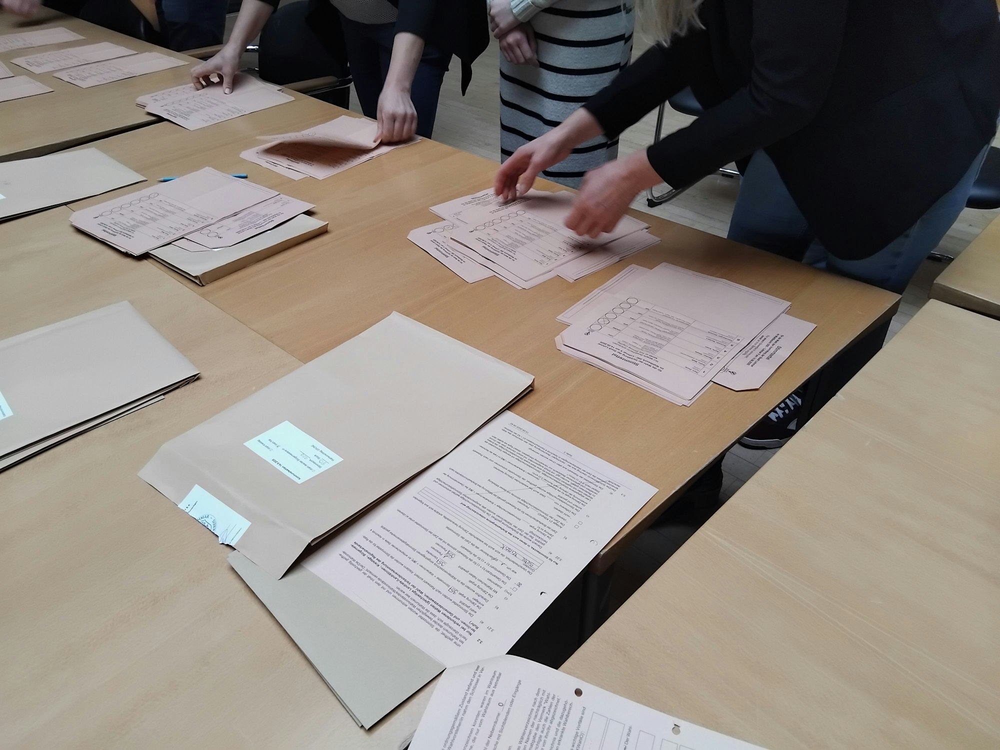 Auf dem Tisch liegen brauen Umschläge und rosafarbene Wahlzettel.