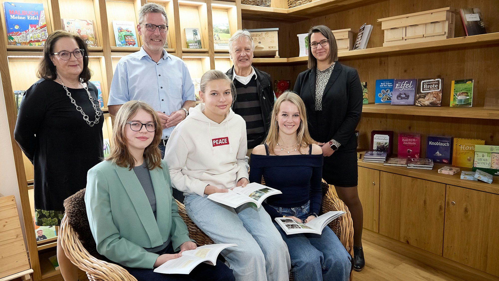 Drei Frauen sitzen auf Stühlen, hinter ihnen stehen die weiteren vier Genannten. Im Hintergrund Regale mit Büchern.