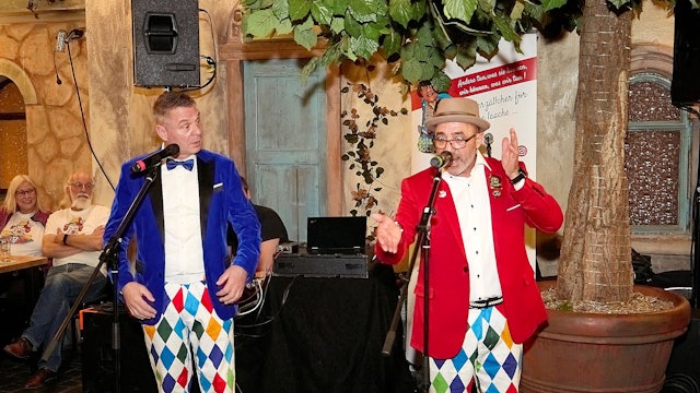 Das Redner-Duo Botz und Bötzje steht in bunten Kostümen an den Mikrofonen.