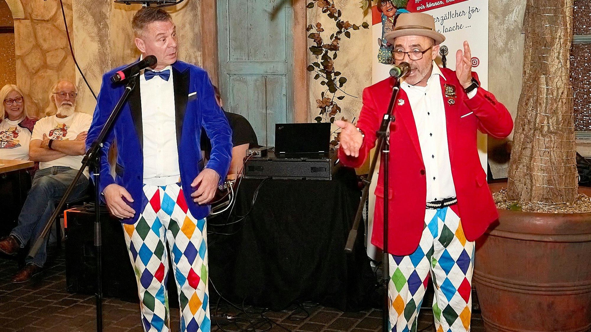 Das Redner-Duo Botz und Bötzje steht in bunten Kostümen an den Mikrofonen.