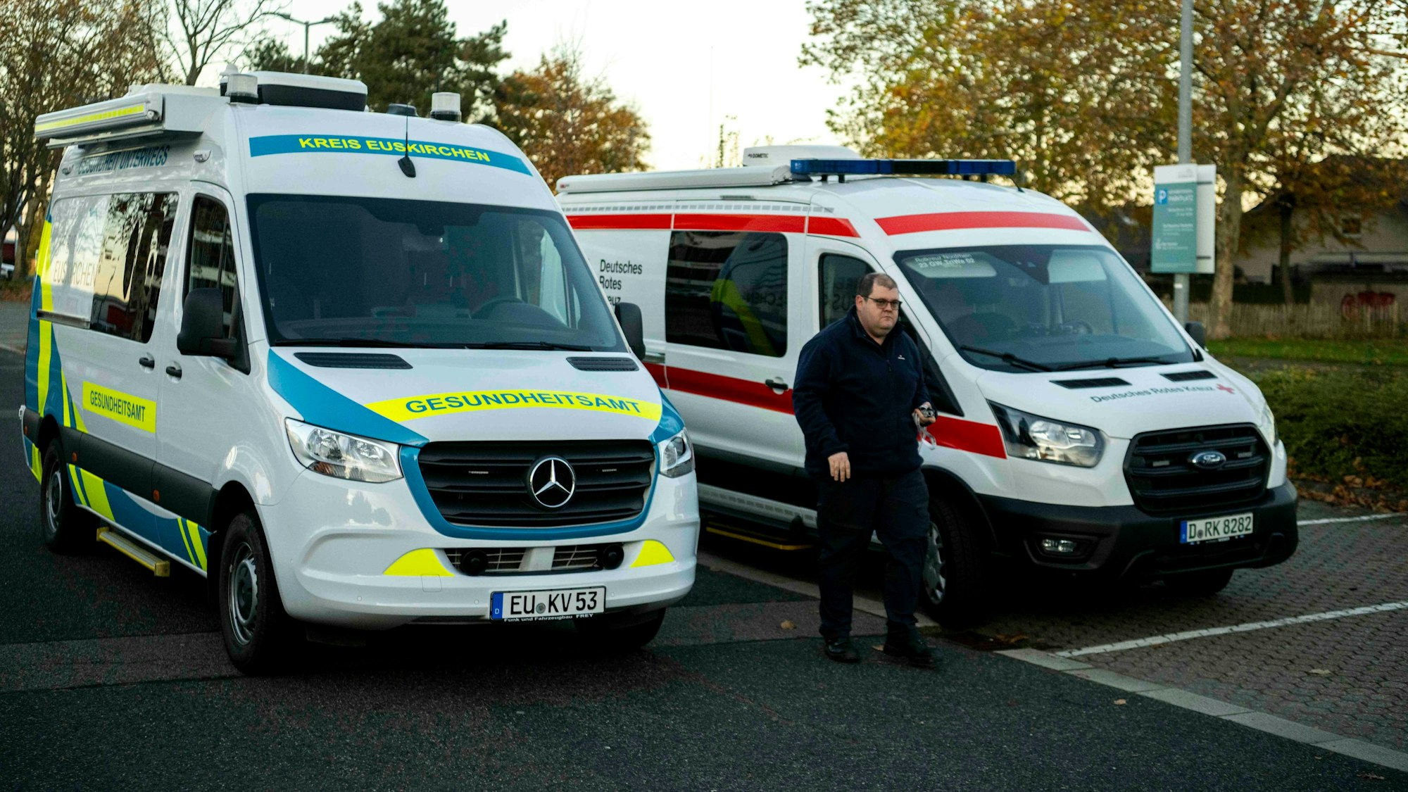 Zwei Fahrzeuge des Gesundheitsamts des Kreises Euskirchen und des Deutschen Roten Kreuzes samt der entsprechenden Beschriftzungen stehen nebeneinander auf einem Parkplatz.