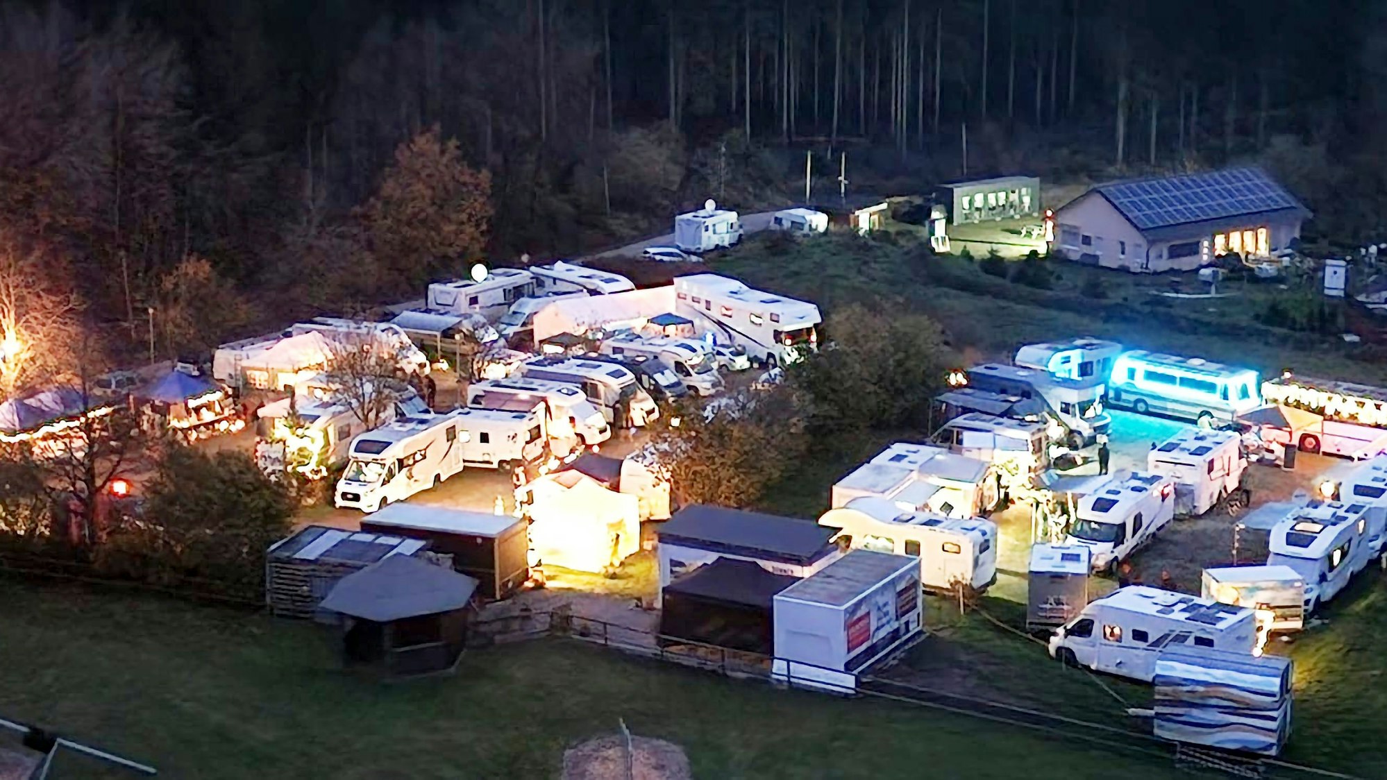 Zwischen Campingwagen stehen mehrere leuchtende Buden.