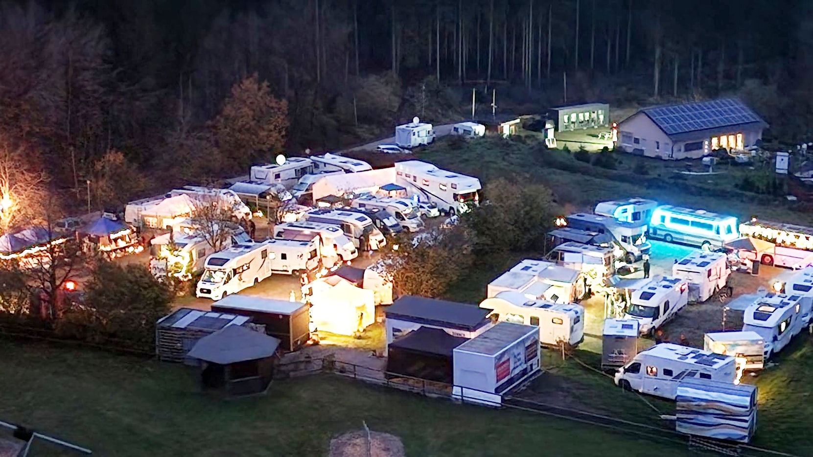 Zwischen Campingwagen stehen mehrere leuchtende Buden.