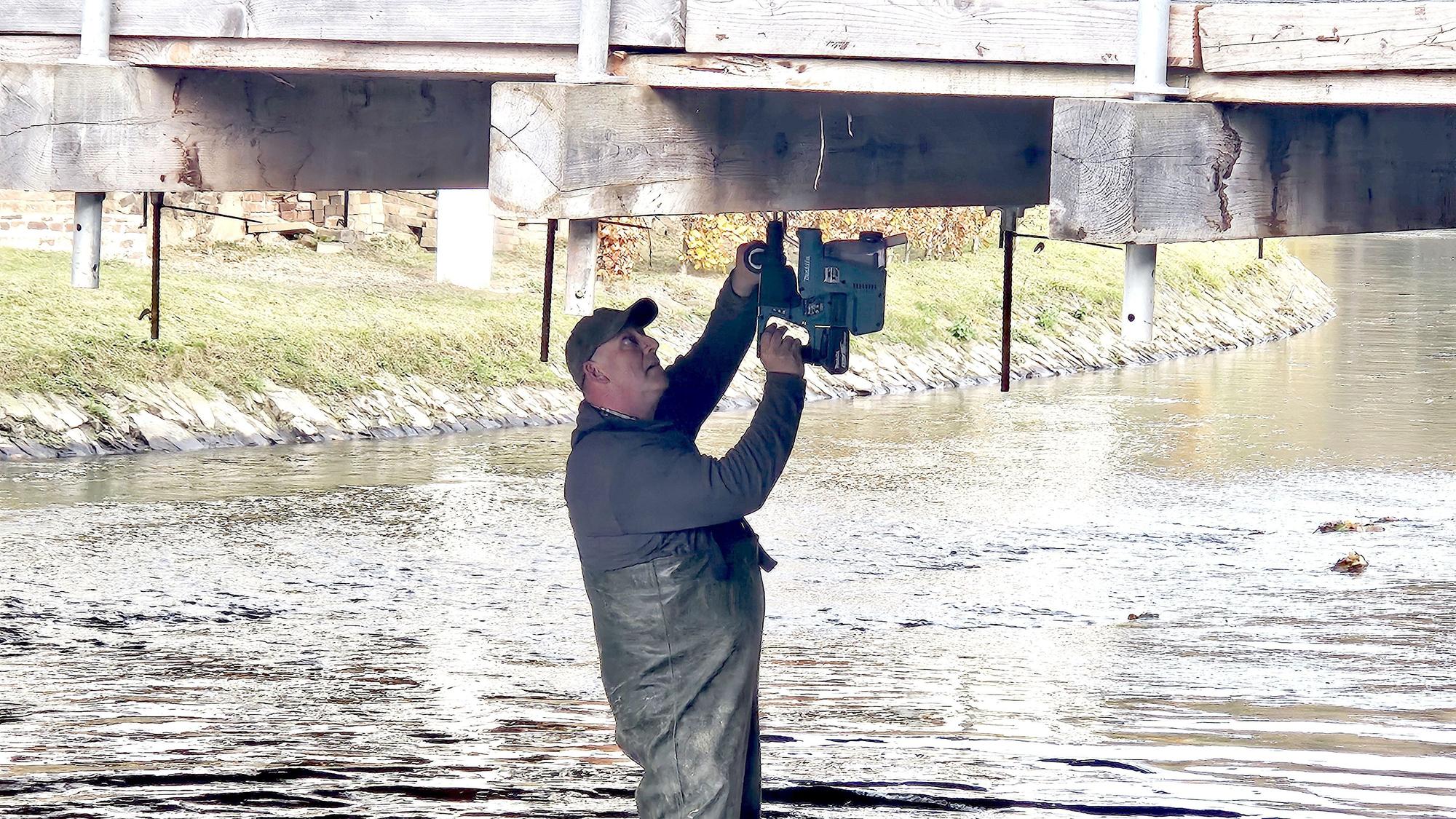 Ein Mann steht in der Olef und bohrt die Unterseite der Brücke an.