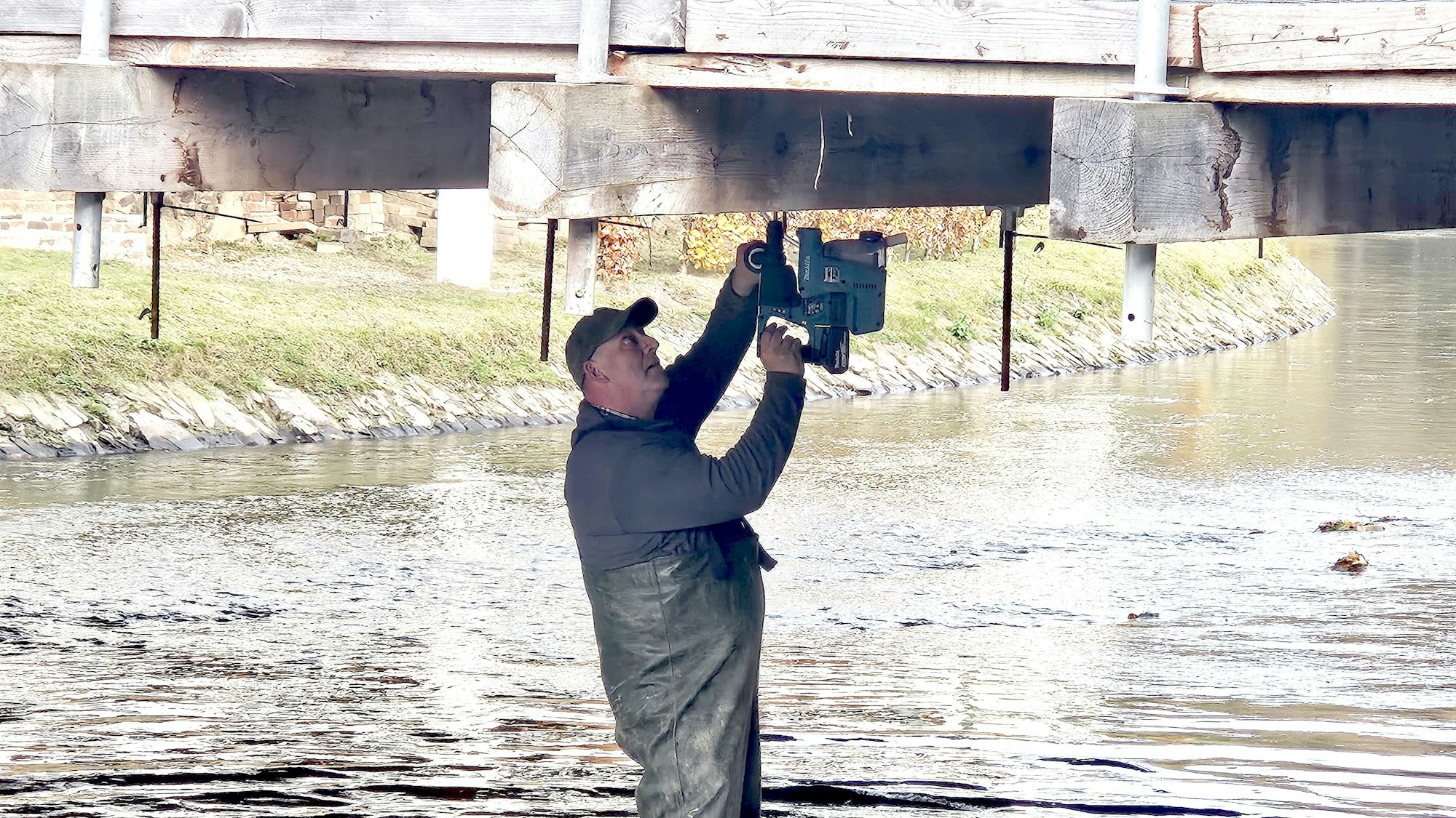Ein Mann steht in der Olef und bohrt die Unterseite der Brücke an.