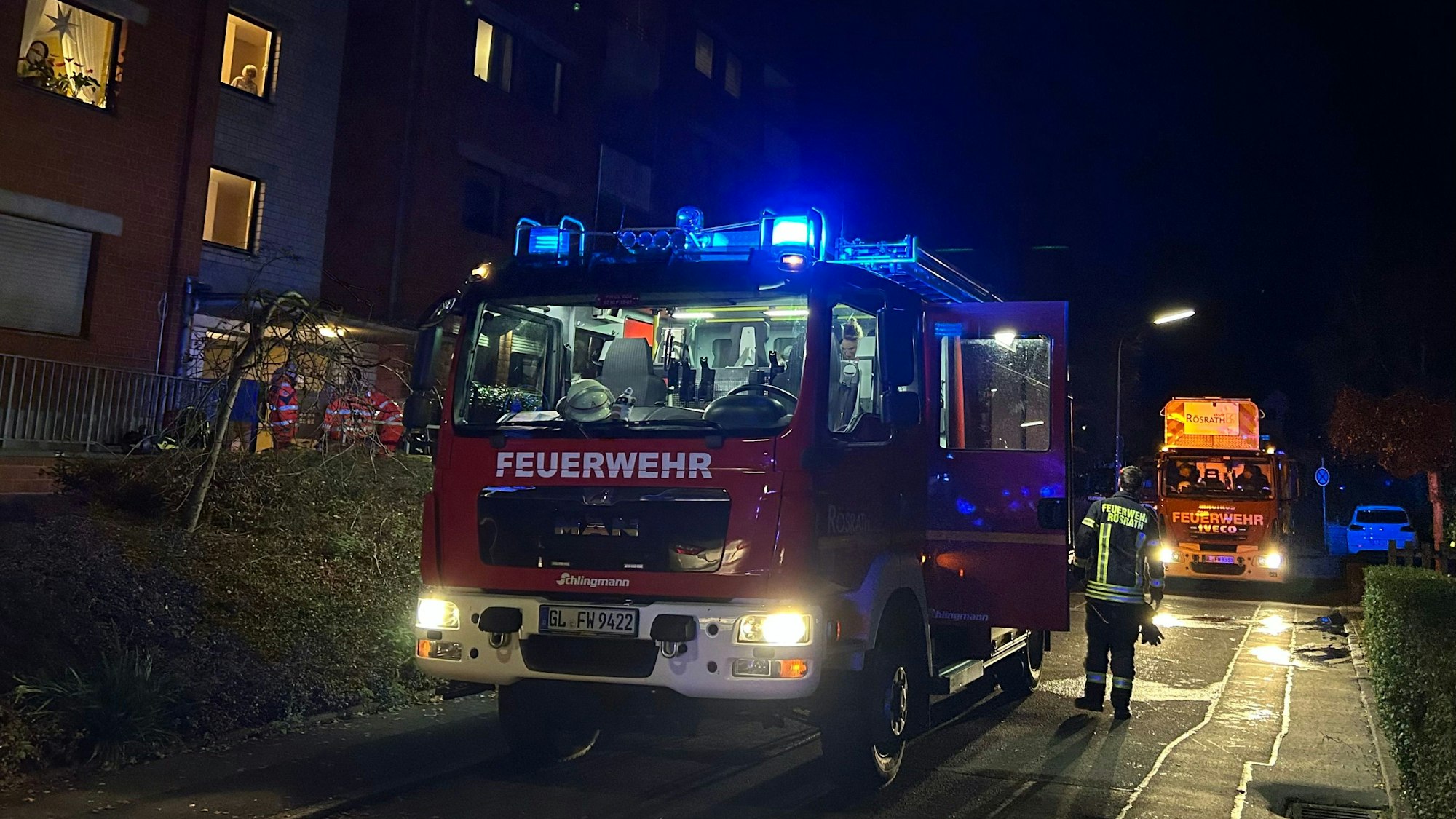 Ein Feuerwehrfahrzeug mit Blaulicht ist im Einsatz vor einem Wohngebäude. Es handelt sich um ein Symbolfoto