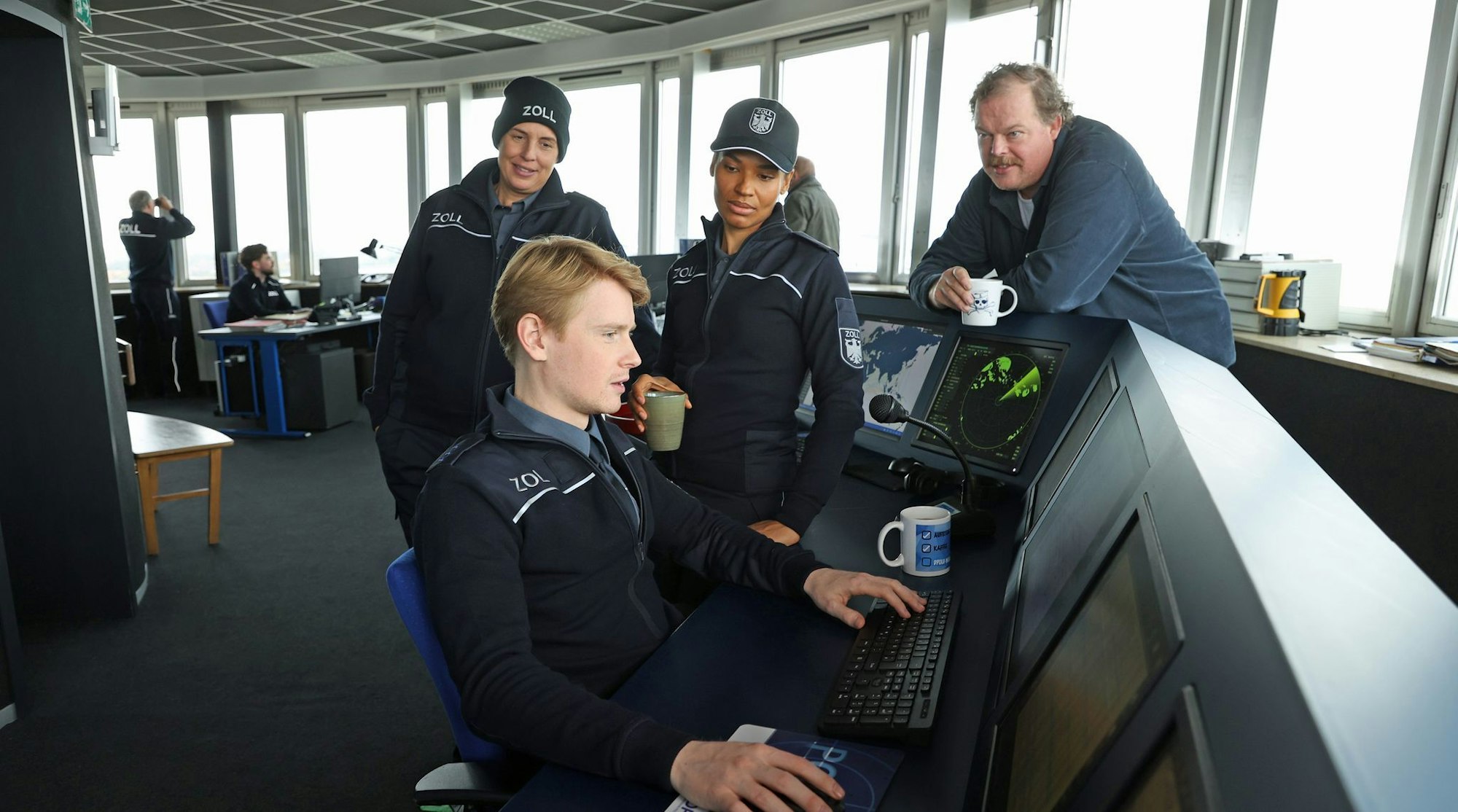 Zöllner Sven-Erik Dröse (Lukas Zumbrock, sitzend) kommt einer heißen Spur auf die Schliche in einer Szene aus der Folge «Geschäft mit dem Tod» aus der Krimireihe «Der Bremerhaven-Krimi» - hinten von links nach rechts: Elena Uhlig, Cynthia Micas, Bernd Hölscher.