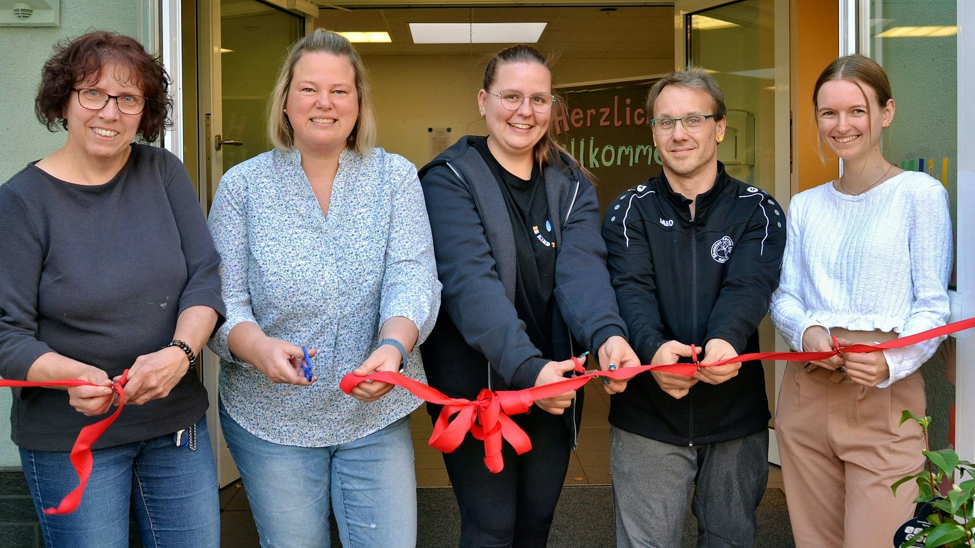 Vier Erzieherinnen und ein Erzieher durchschneiden gemeinsam ein rotes Band.
