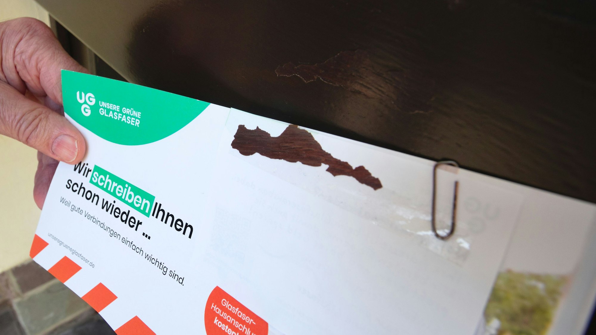 Ein Mann hält einen Flyer neben seiner Haustüre. Es ist zu sehen, dass am Flyer braune Farbe klebt, die an der Haustüre fehlt.