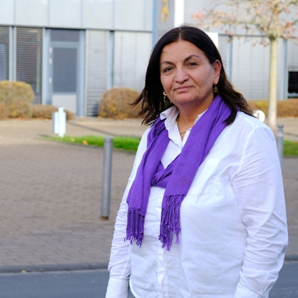 Die Mechernicher Lokalpolitikerin Zizik (genannt: Zosan) Sahbaz steht vor dem Mechernicher Rathaus. Sie trägt eine weiße Bluse und einen lilafarbenen Schal.