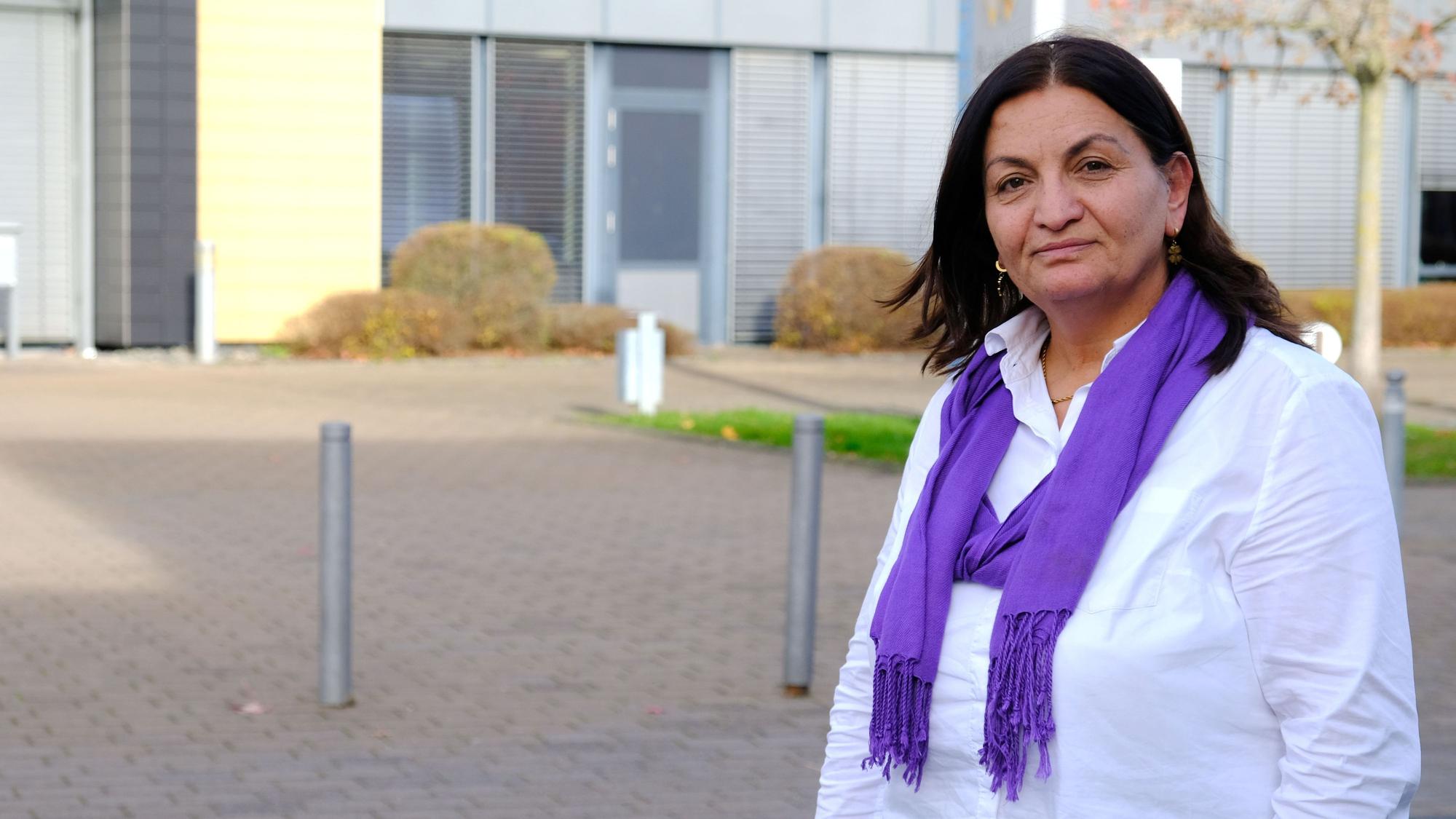 Die Mechernicher Lokalpolitikerin Zizik (genannt: Zosan) Sahbaz steht vor dem Mechernicher Rathaus. Sie trägt eine weiße Bluse und einen lilafarbenen Schal.