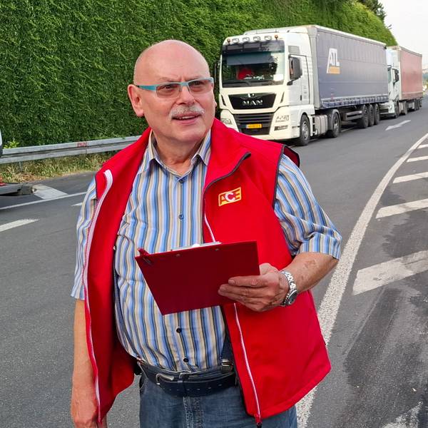 Auf dem Bild ist ein Mann an einer Autobahn-Raststätte zu sehen. Im Hintergrund parken Lkw.