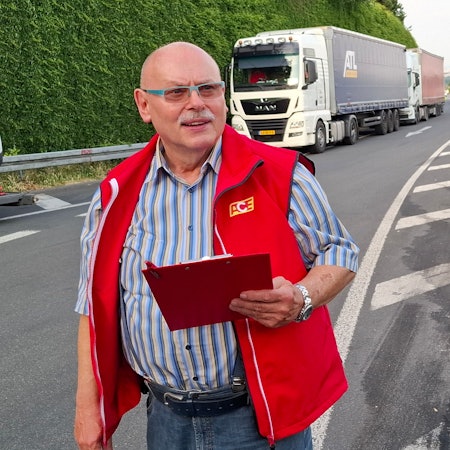 Auf dem Bild ist ein Mann an einer Autobahn-Raststätte zu sehen. Im Hintergrund parken Lkw.