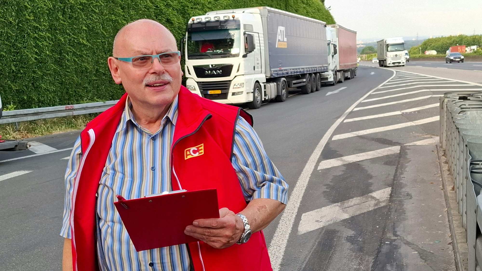 Auf dem Bild ist ein Mann an einer Autobahn-Raststätte zu sehen. Im Hintergrund parken Lkw.