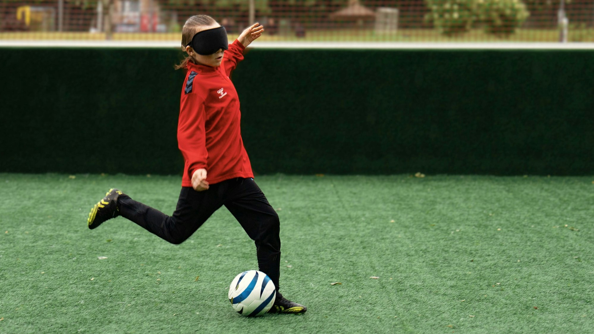 Zu sehen ist ein junger Blindenfußballer, der vor den Ball tritt.