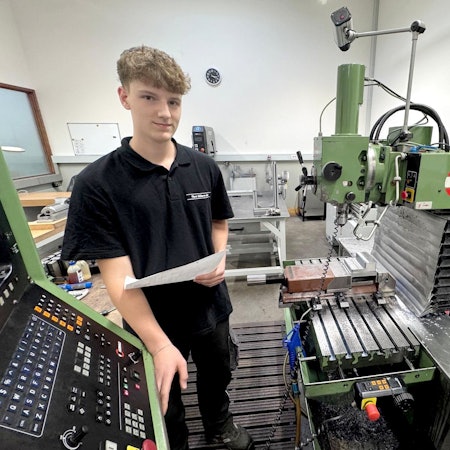 Jason Epp steht neben einer Fräsmaschine und hält ein Stück Papier in der Hand.