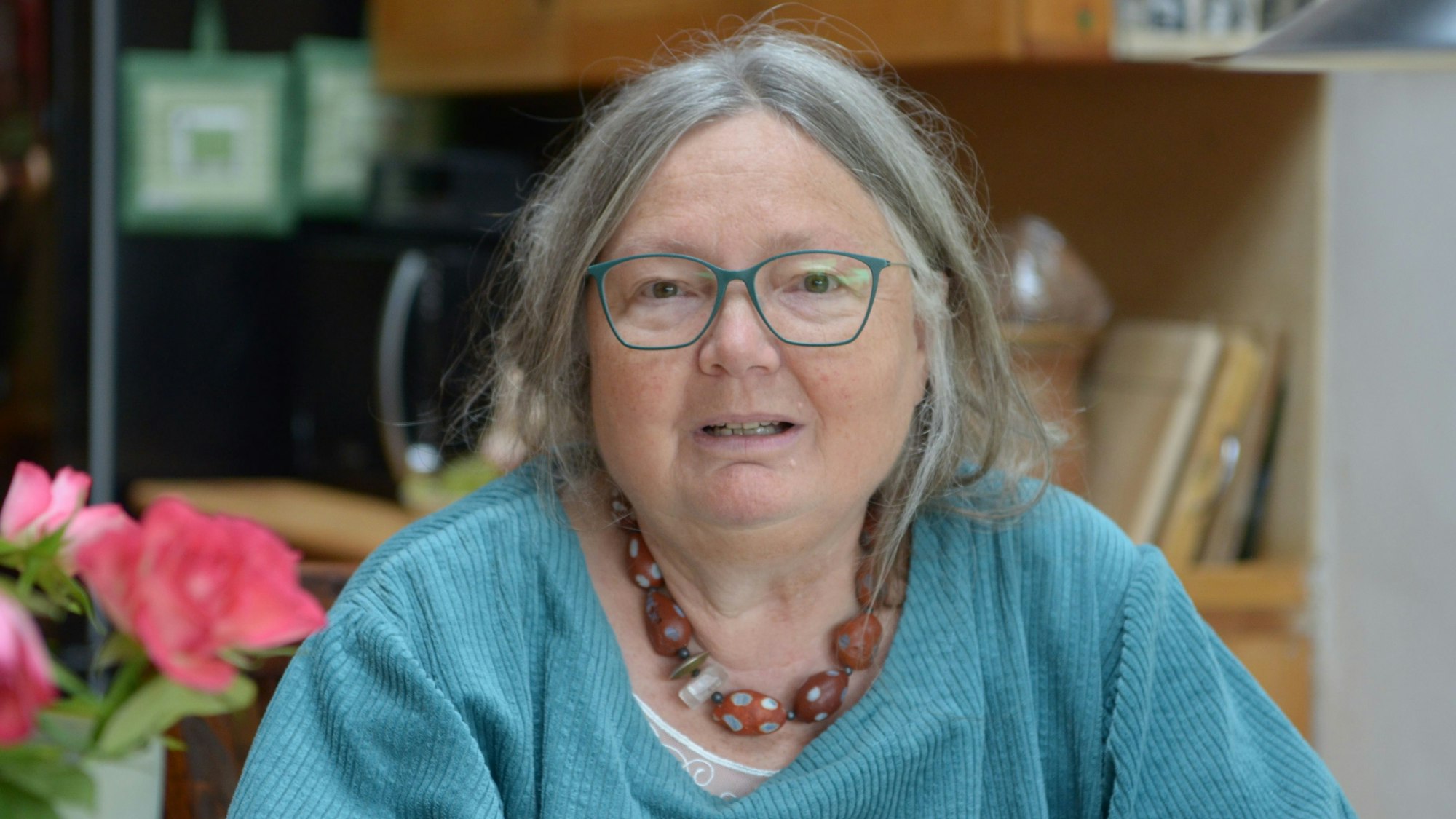 Dorothee Kroll sitzt vor einem Regal, links im Bild sind Blumen zu sehen.