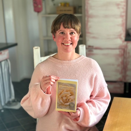 Eine Frau in einem rosafarbenen Pullover hält ein Buch.