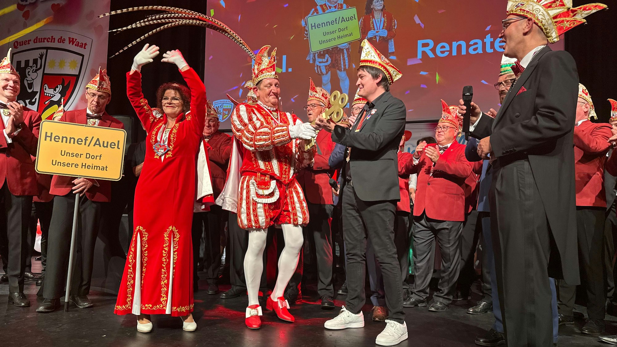Skeptisch schaut Prinz Uli I., als ihm Bürgermeister Mario Dahm den Schlüssel fürs Rathaus bei der Prinzenproklamation 2025 in Hennef übergibt, Renate I. jubelt. Moderator Jörg Steinhauer (r.) freut sich.