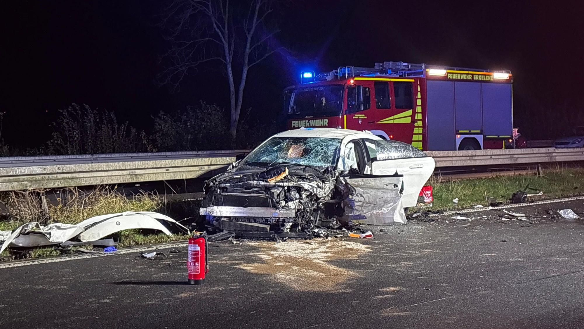 Ein schwer beschädigtes Auto steht vor einem Einsatzfahrzeug der Feuerwehr auf der Autobahn 46 bei Heinsberg.