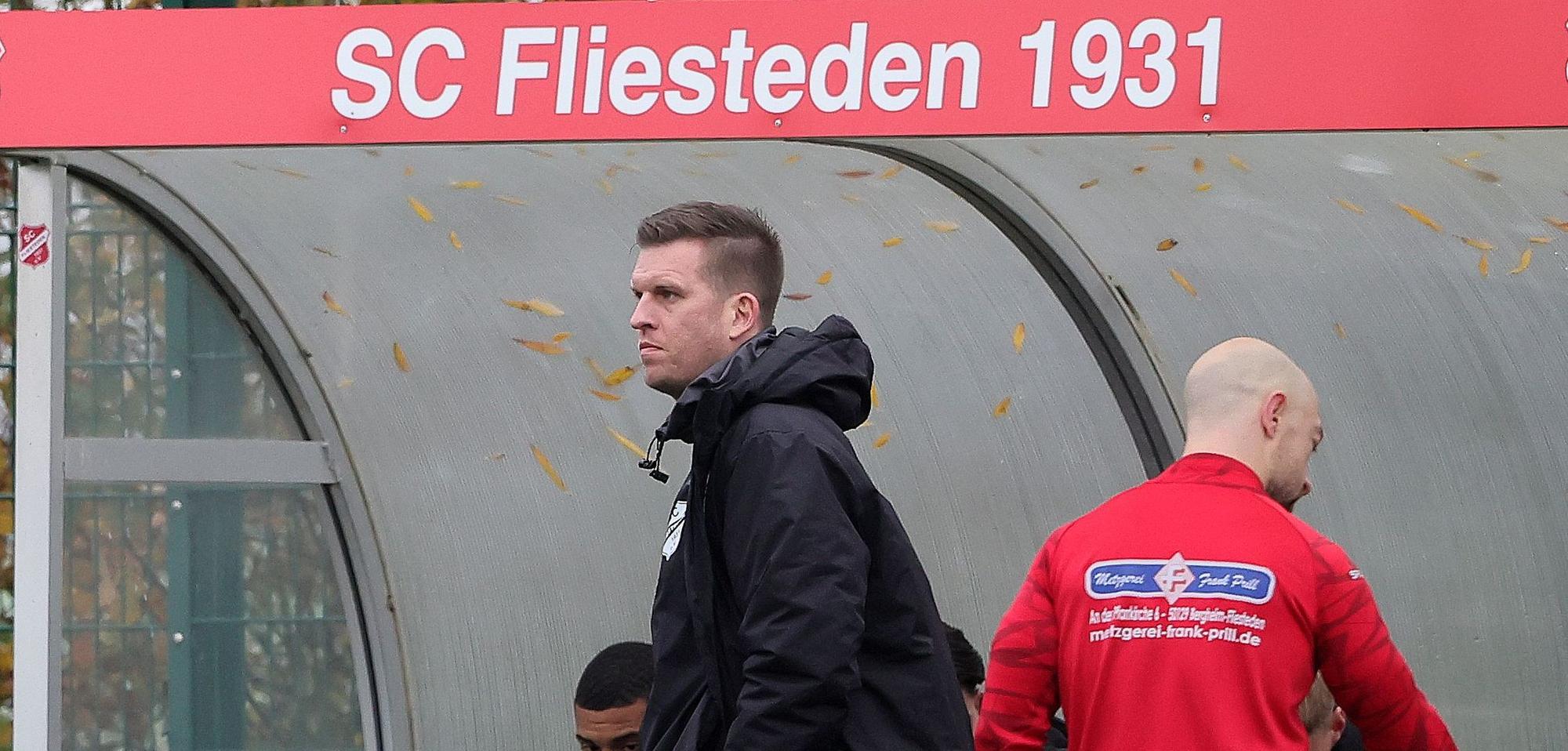 Das Foto zeigt den neuen Fliestedener Trainer vor seiner Bank mit dem Vereinsnamen.