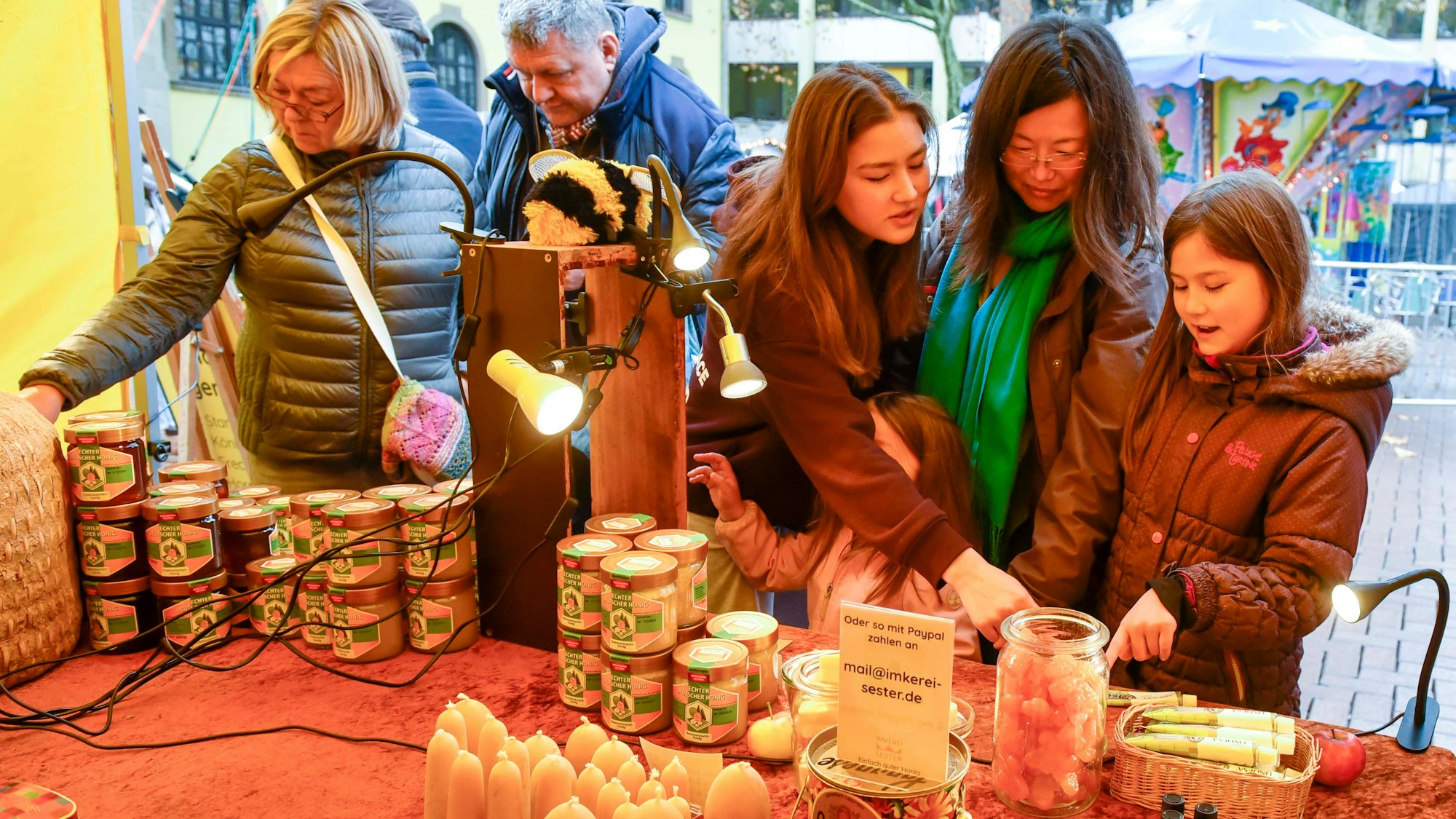 Zu sehen sind Menschen an einem Stand, an dem Honig angeboten wird.