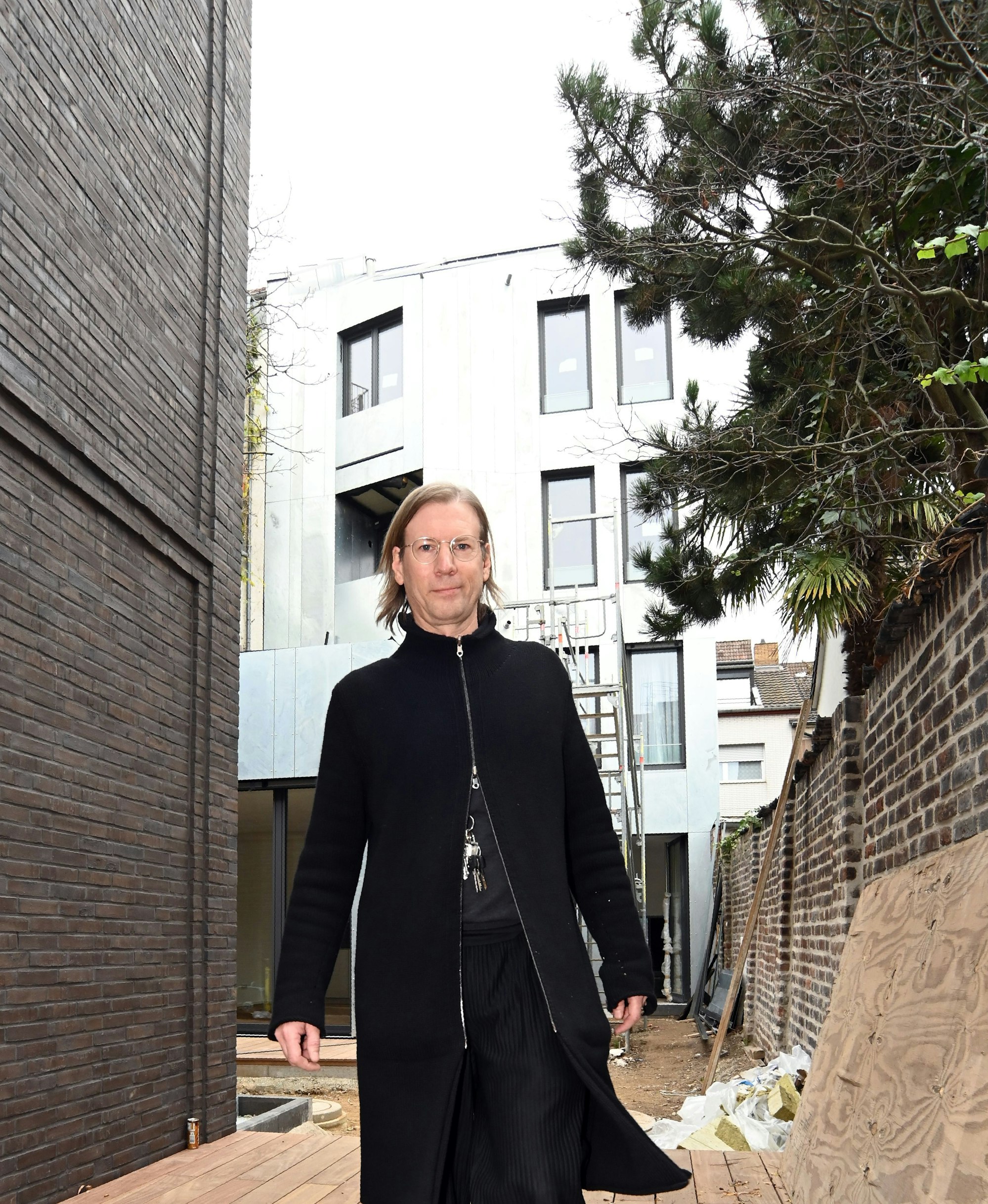 Ein Mann im schwarzen Mantel geht durch einen Innenhof, auf dem neue Häuser gebaut wurden.