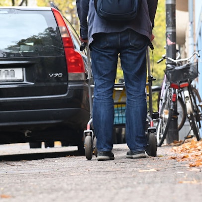 20.10.2025 Köln. Ein PKW parkt auf der Melchiorstraße soweit auf dem Gehweg, daß ein Herr mit Rollator auf die Straße ausweichen muss. Foto: Alexander Schwaiger