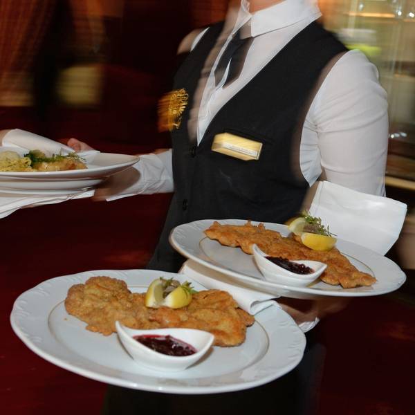 Eine Servicekraft trägt drei Teller mit Schnitzeln durch ein Restaurant.