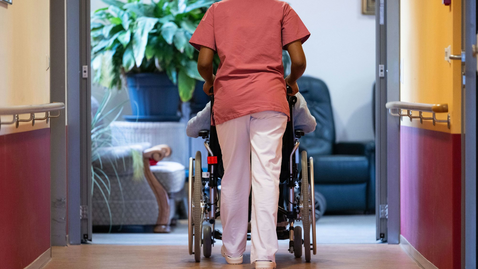 Das Bild zeigt eine Bewohnerin eines Pflegeheims, die von einer Pflegerin einen Gang entlang geschoben wird. Foto: Marijan Murat/dpa