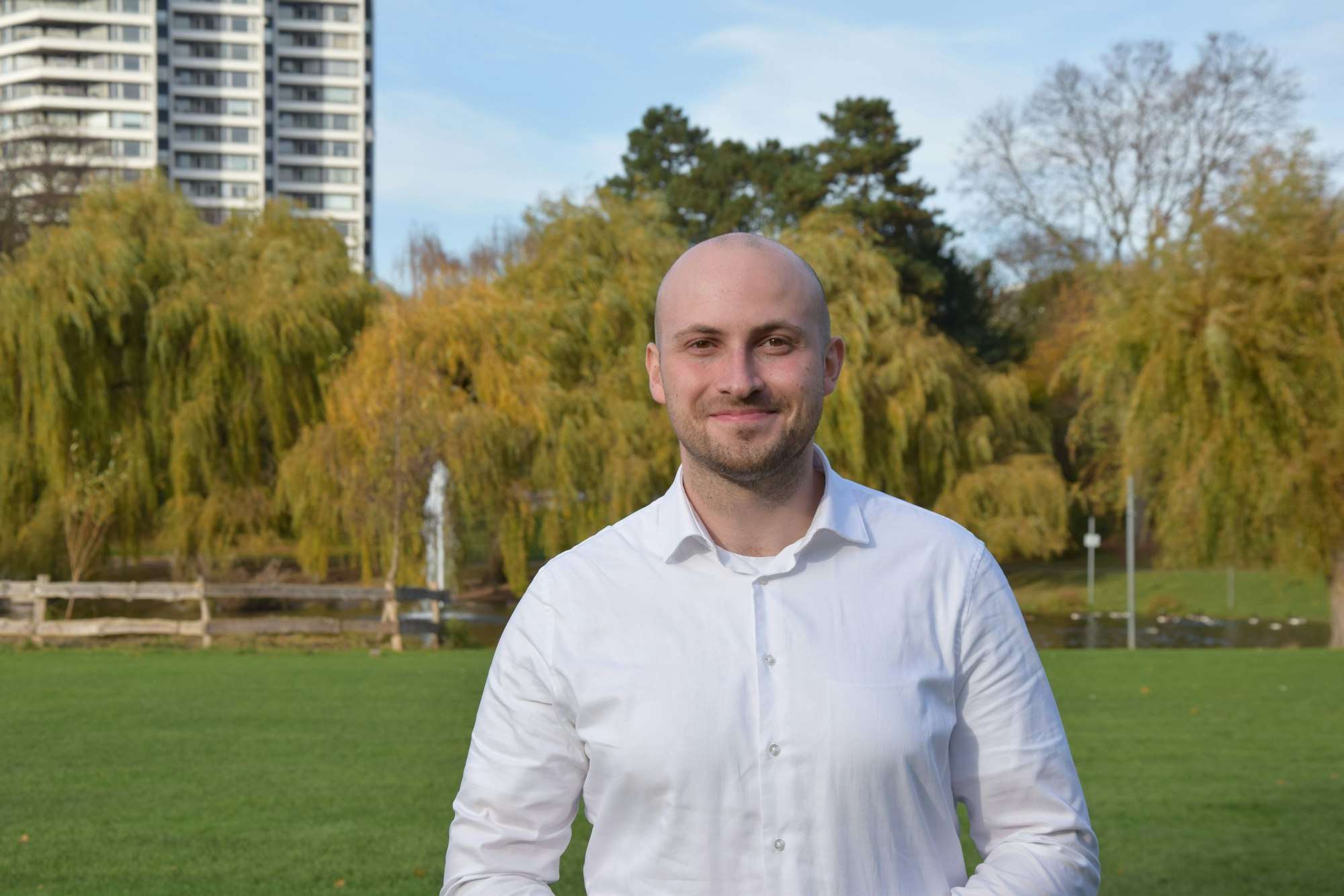 Ein junger Mann im weißen Hemd steht auf einer Wiese vor einem Teich.