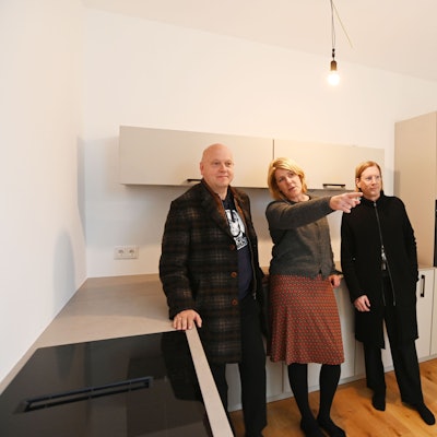 Drei Menschen stehen an eine Küchenzeile gelehnt in einem Haus.