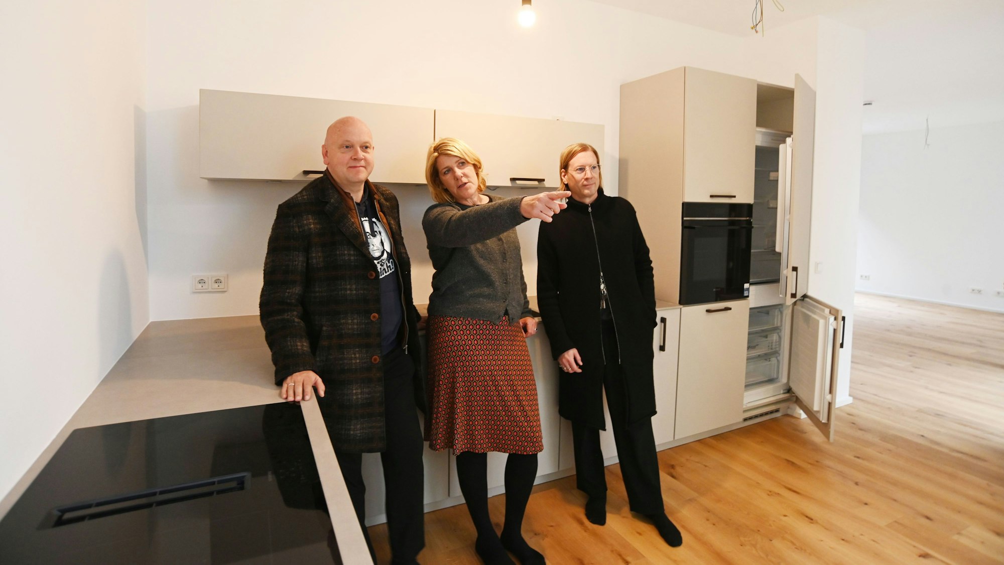 Drei Menschen stehen an eine Küchenzeile gelehnt in einem Haus.