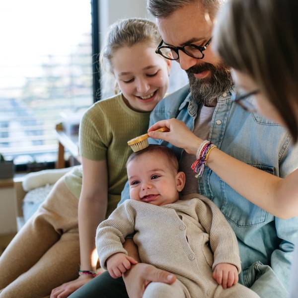 Eine junge Familie sitzt zusammen mit einem Baby und einer Erziehungshelferin auf dem Sofa. Sie kämmt das kleine Kind.
