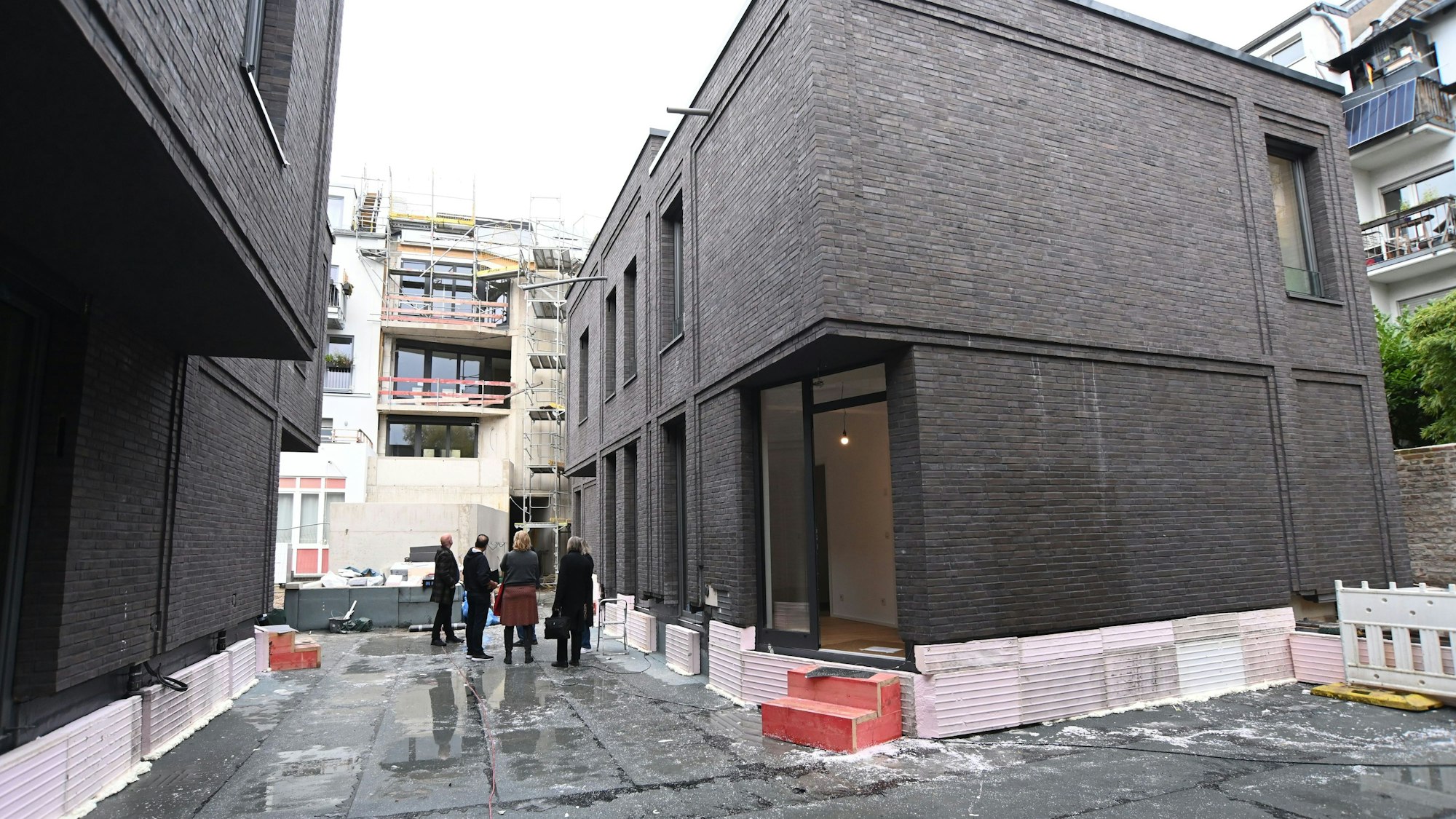 Eine Menschengruppe steht in einem Innenhof, die Häuser sind noch Baustelle.