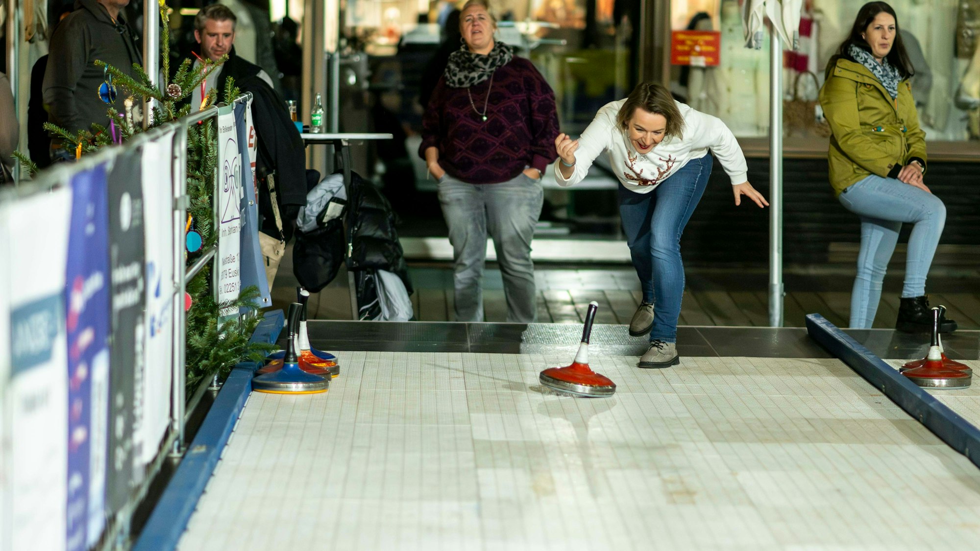 Eine Frau in Jeans und weißem Shirt probiert die Bahn zum Eisstockschießen in Euskirchen aus.