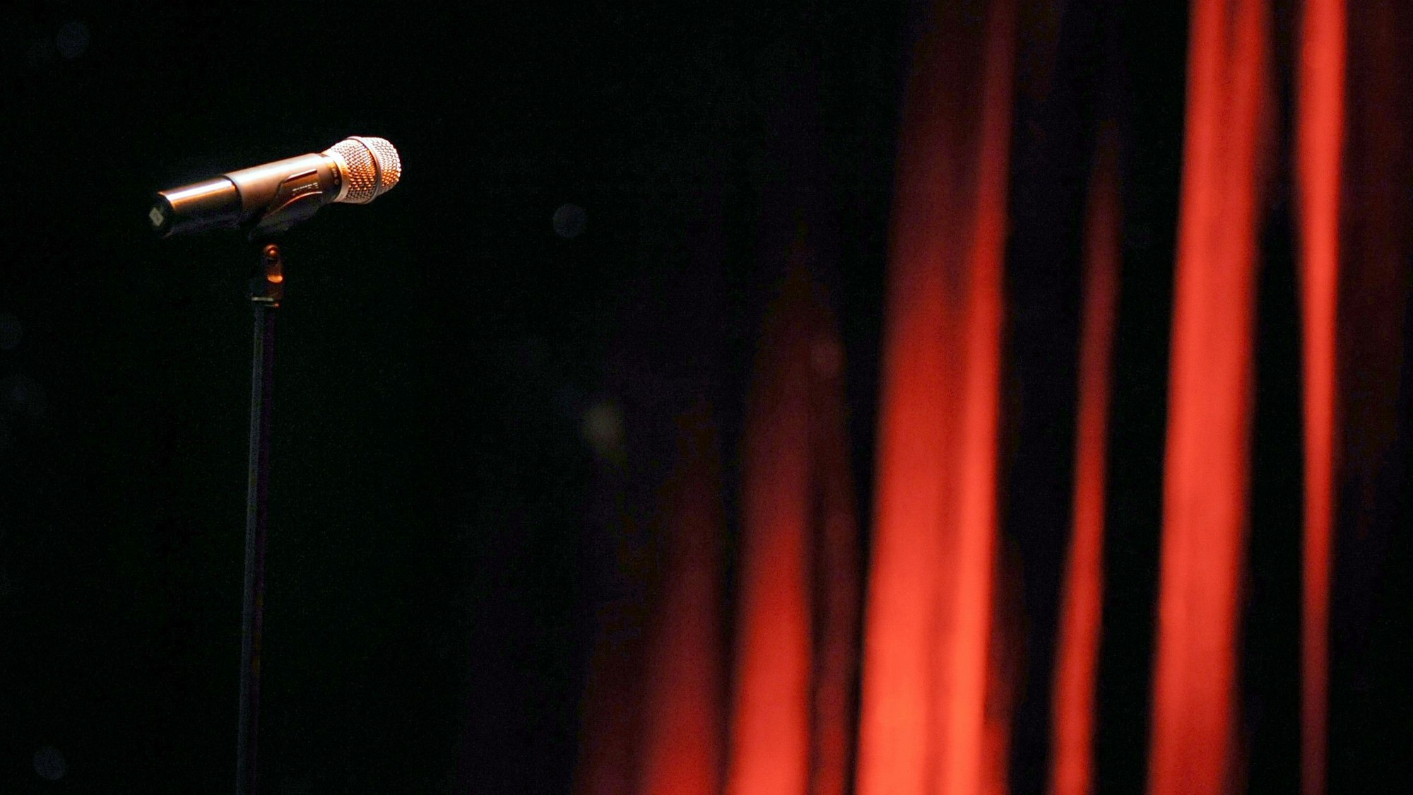 Ein Mikrofon steht in einem Theater vor einem roten Vorhang. (Symbolbild)