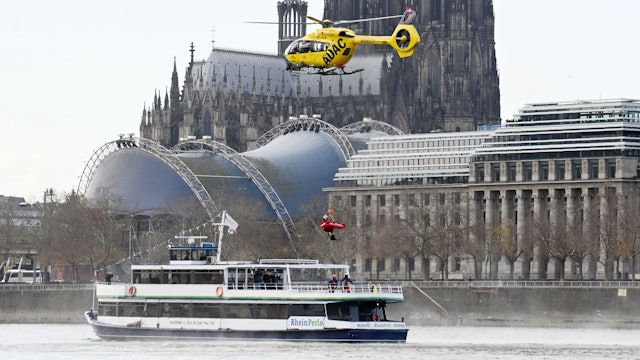 Ein ADAC-Hubschrauber schwebt auf dem Rhein vor dem Dom über einem Schiff, an seiner Winde hängt ein Retter mit einer Trage.