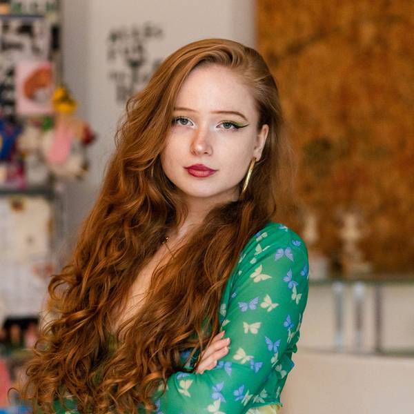 Eine junge Frau mit roten Locken und grünem Kleid schaut in die Kamera.