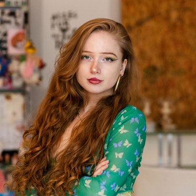 Eine junge Frau mit roten Locken und grünem Kleid schaut in die Kamera.