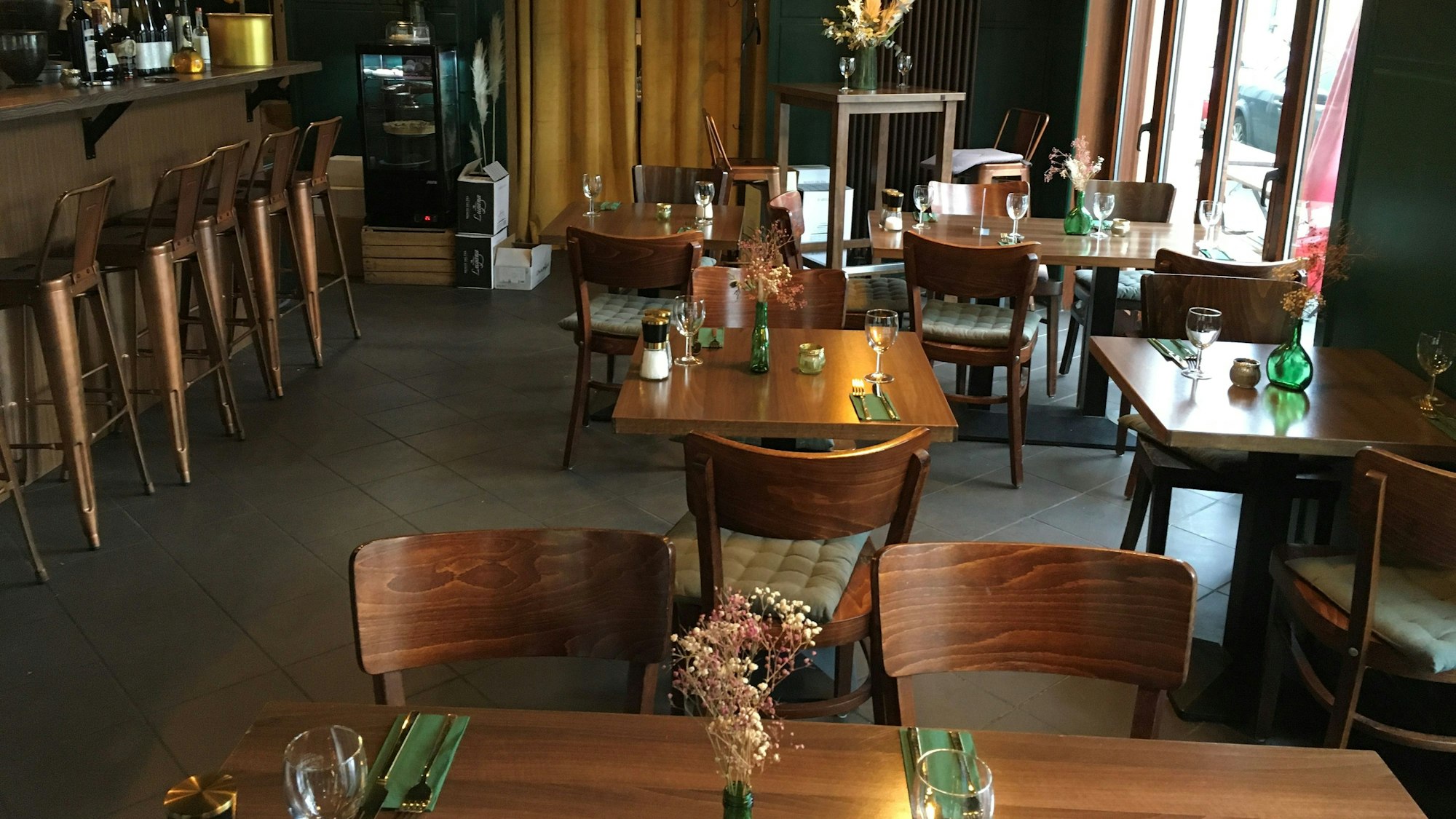 Das Interieur im Weinlokal JuBo: Holztische und Holzstühle, schwarze Lampen und links eine Theke.