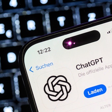 Ein Smartphone mit der App des KI-Chatbots ChatGPT ist vor dem Logo des US-Softwareunternehmens OpenAI zu sehen.