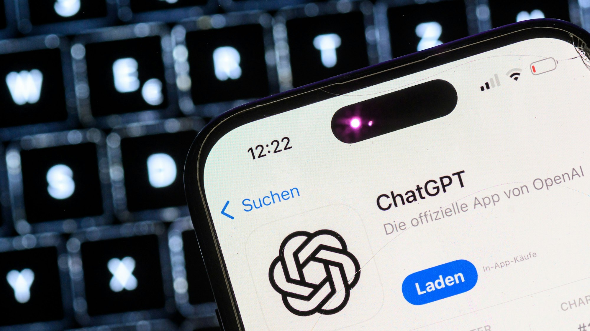 Ein Smartphone mit der App des KI-Chatbots ChatGPT ist vor dem Logo des US-Softwareunternehmens OpenAI zu sehen.
