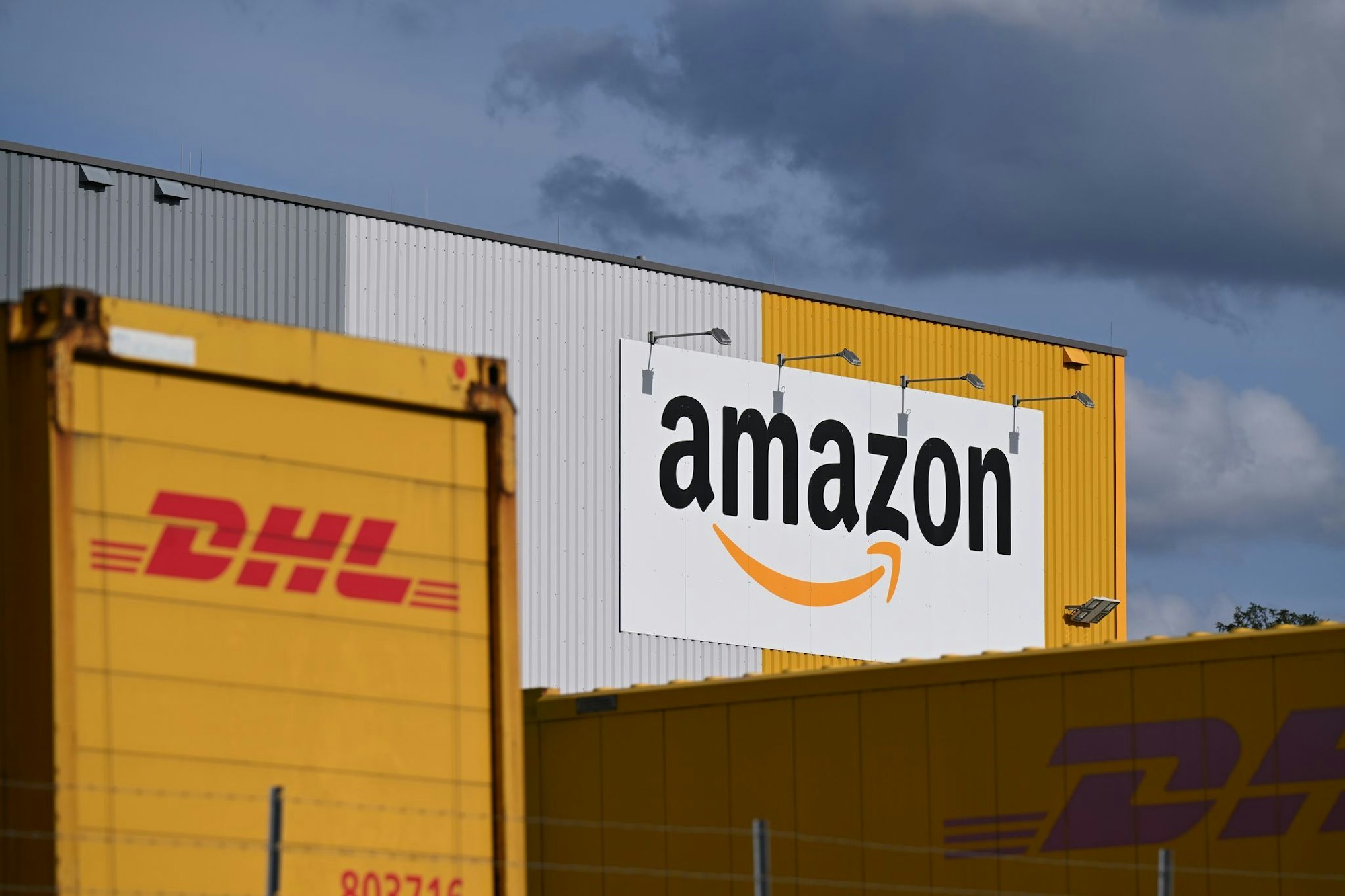 Ein Logistikzentrum von Amazon, auf dessen Gelände DHL-Container stehen. DHL ist das größte Paketunternehmen in Deutschland, gefolgt von Amazon - der Online-Handelsriese trägt einen großen Teil bei ihm bestellten Waren selbst aus. (Archivbild)