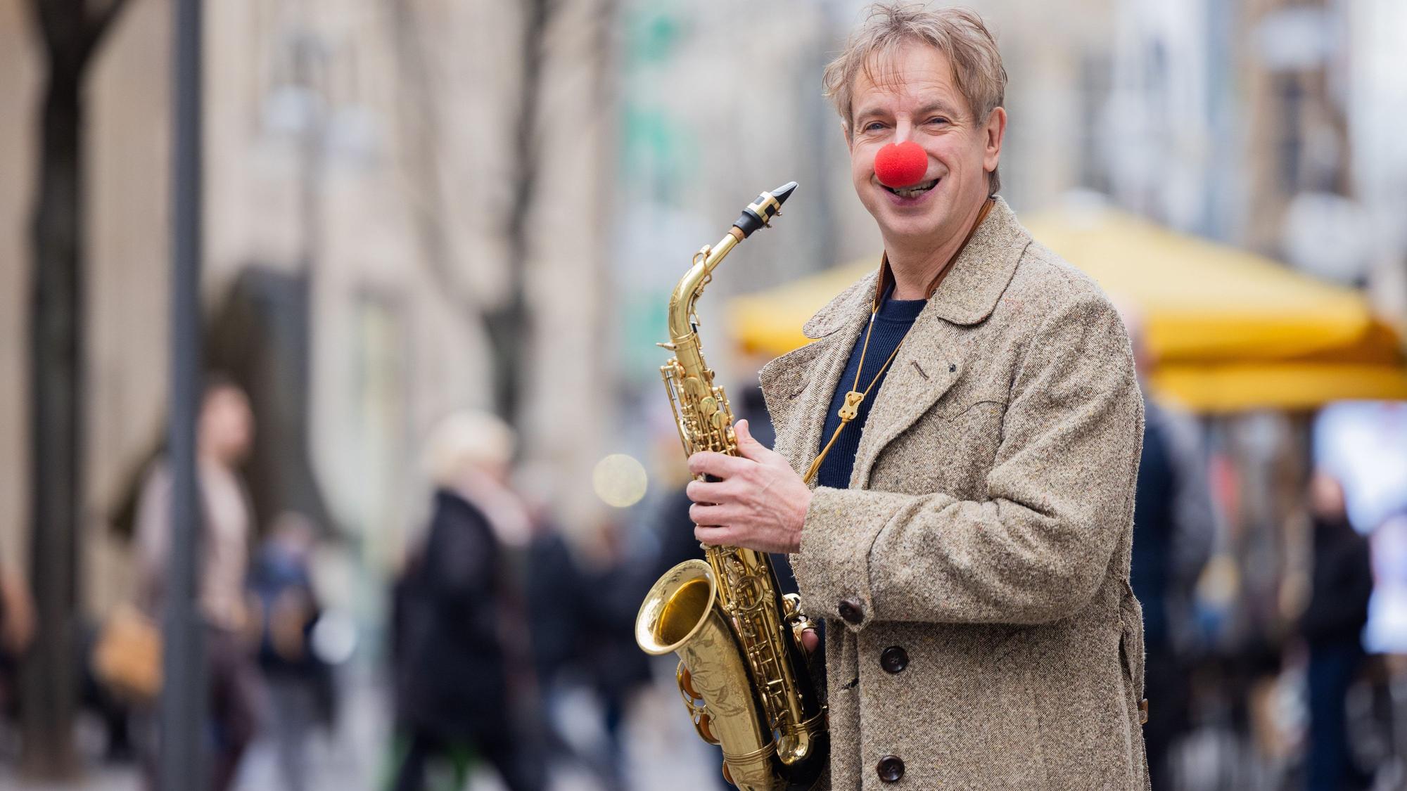 Ingolf Lück mit Saxophon auf einer Einkaufsstraße. Er ist Schauspieler, Moderator, Komiker.