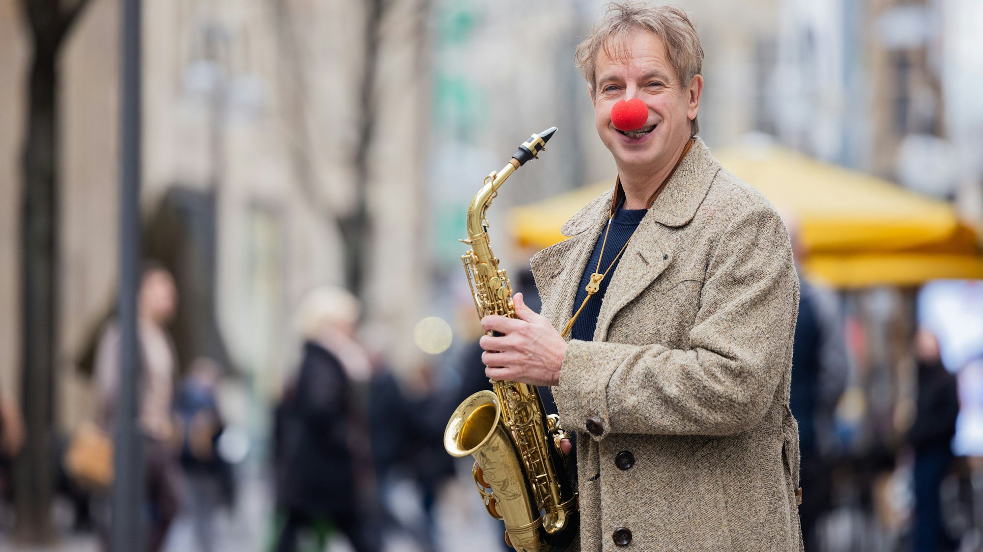 Ingolf Lück mit Saxophon auf einer Einkaufsstraße. Er ist Schauspieler, Moderator, Komiker.