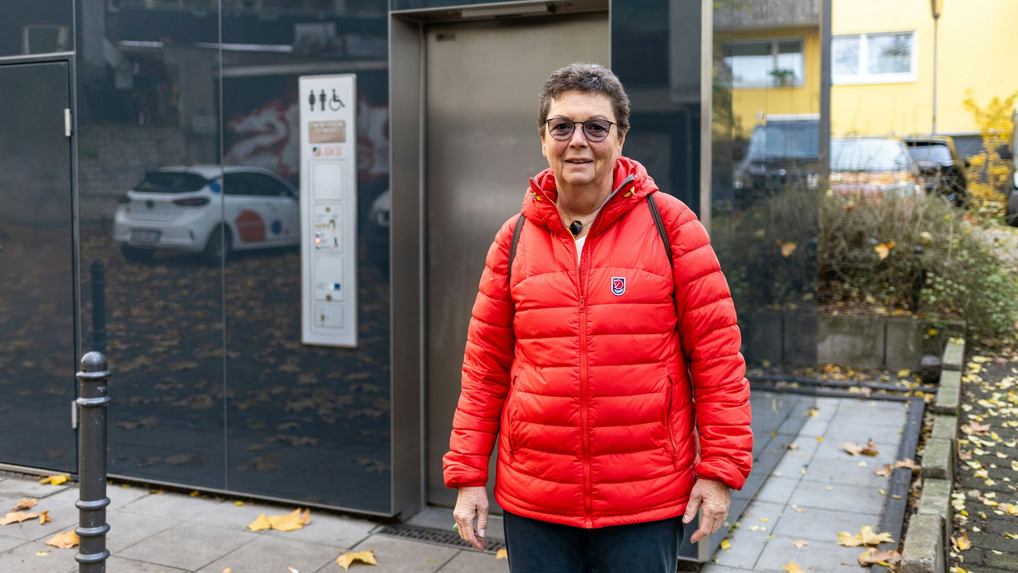 Eine Frau in roter Jacke steht vor einer öffentlichen Toilette.