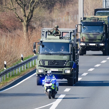 Das Symbolbild zeigt eine Kolonne mit Fahrzeugen der Bundeswehr und schwer bewaffneten Soldaten auf der Autobahn A2 im Norden von Hannover mit einem vorausfahrenden Polizeimotorrad.