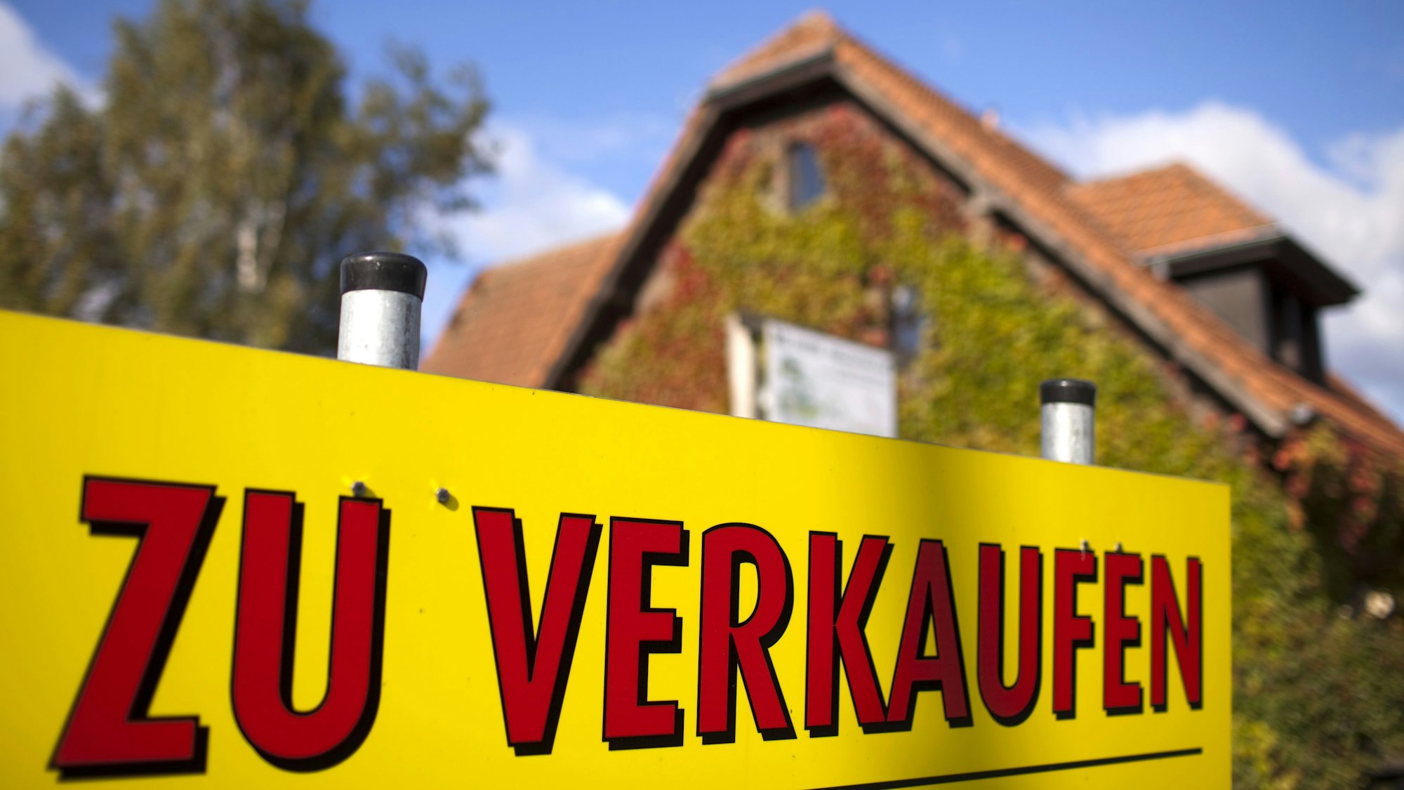 Ein Schild "Zu verkaufen" steht vor einem Haus