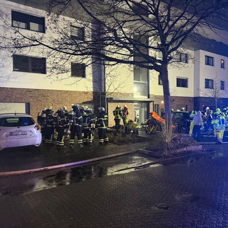 Das Foto zeigt Feuerwehrleute und ein Einsatzfahrzeug mit Blaulicht vor dem Mehrfamilienhaus.